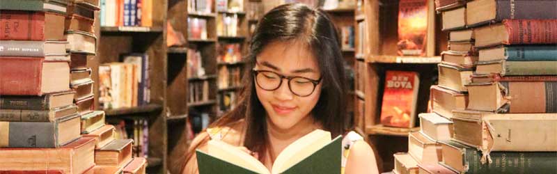 Teen reading surrounded by stacks of books.